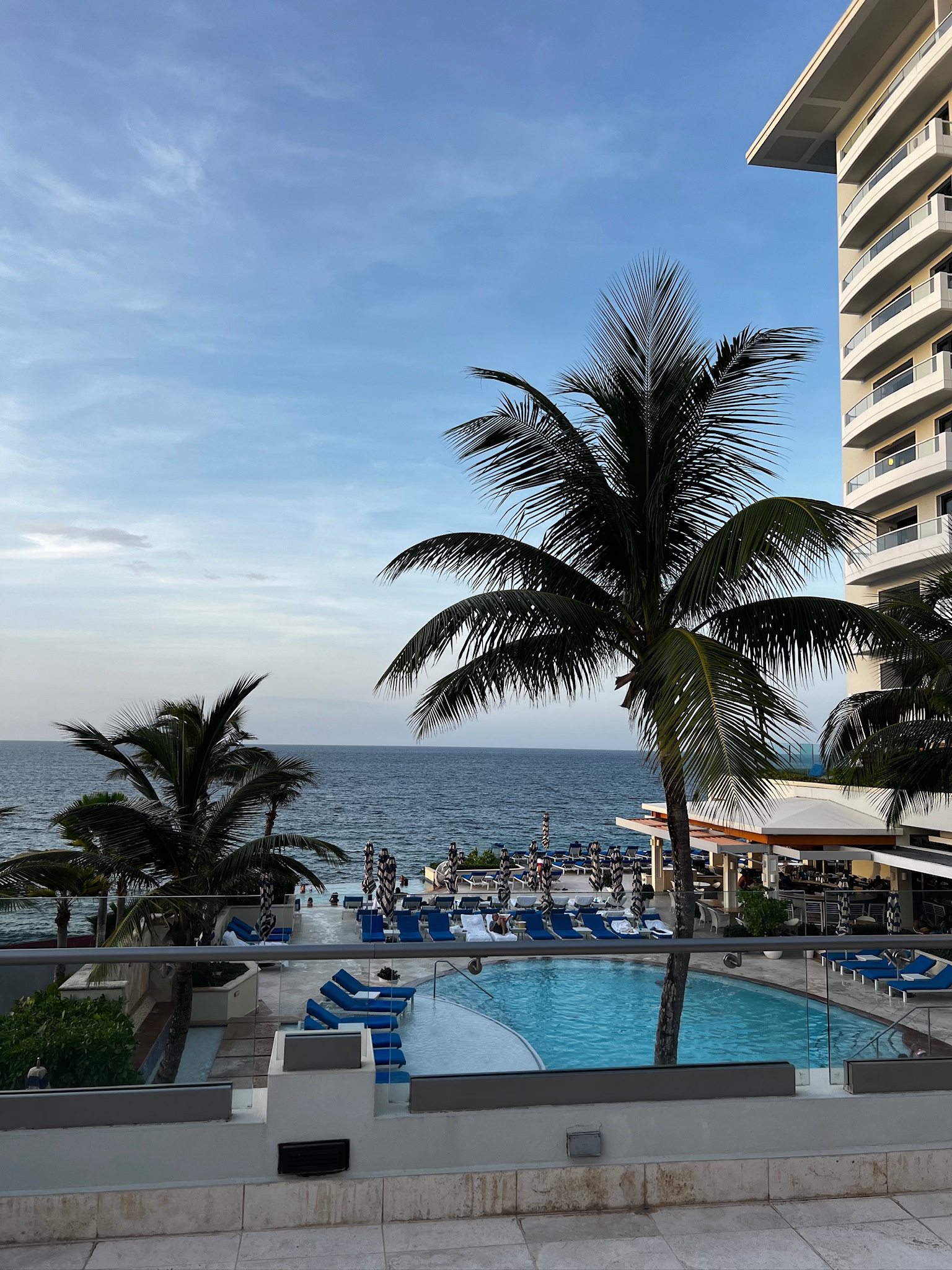 beach island resort with a pool, lunge chairs, and palm trees. in puerto rico overlooking the ocean