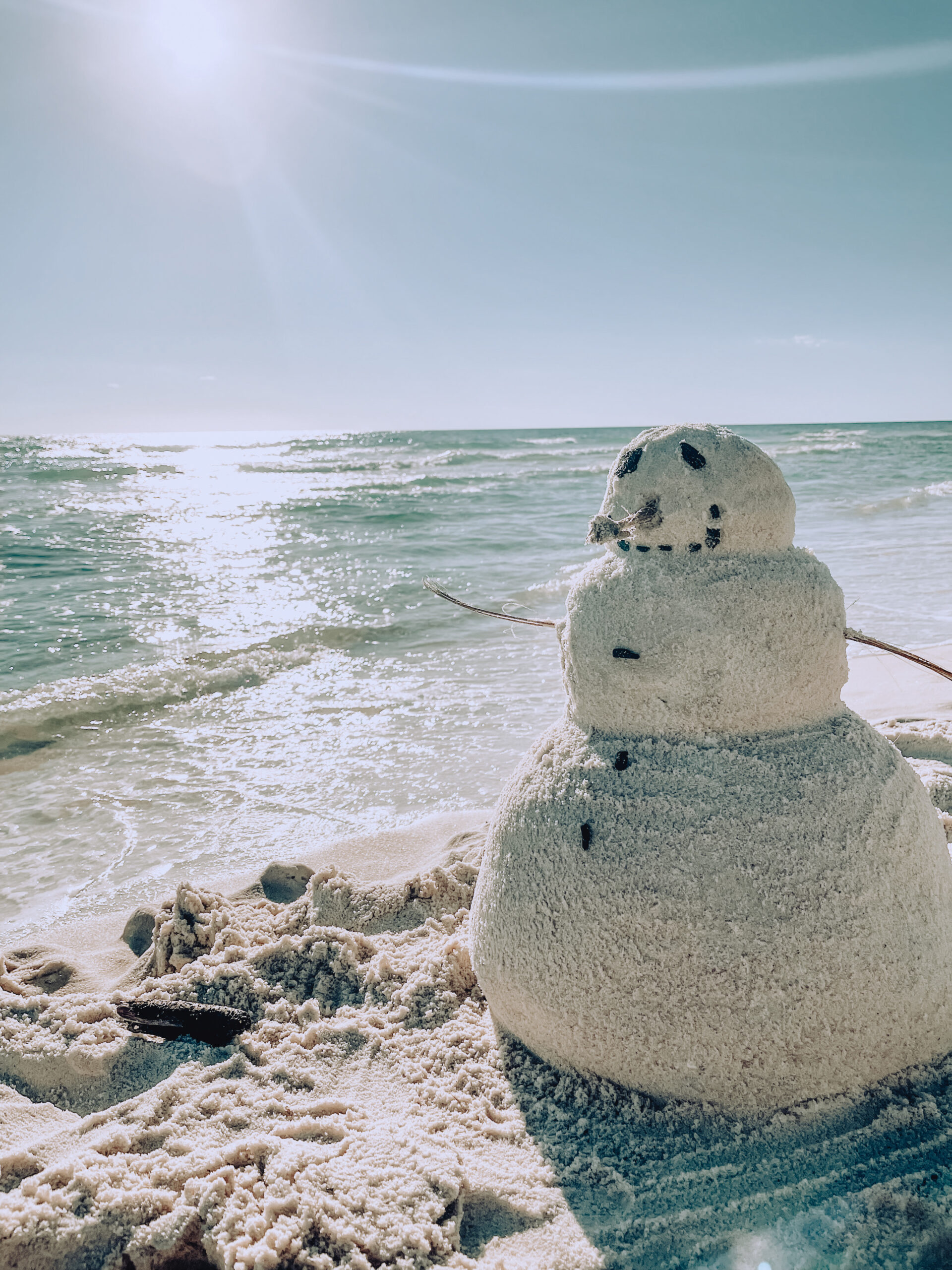 A "snow"man made of sand, on the beach. looking out to the ocean